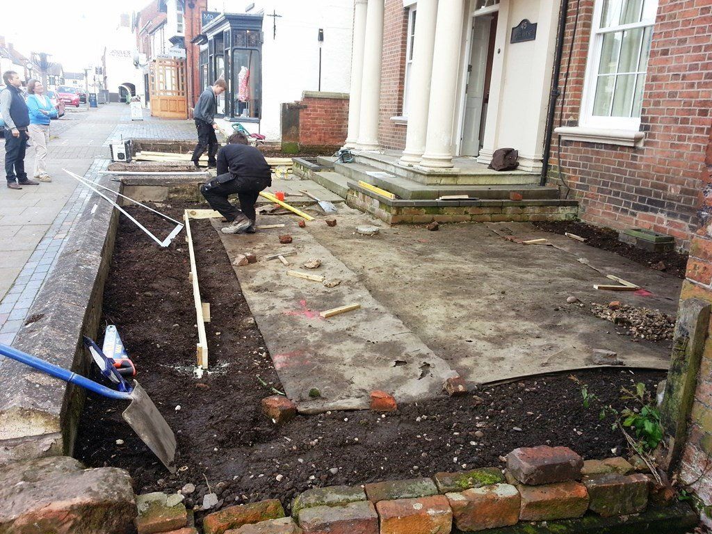 A group of people are working on a sidewalk in front of a brick building.