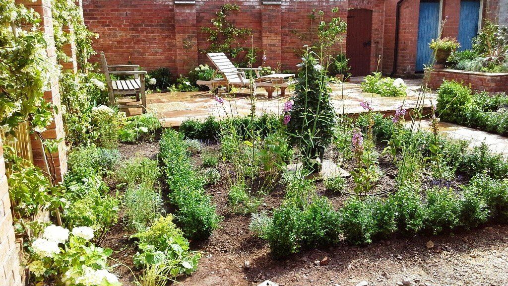 A garden with a bench and chairs in it and a brick wall in the background.