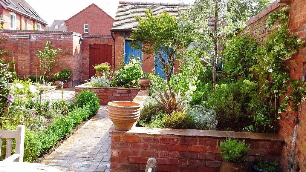 A brick wall surrounds a garden with lots of plants and trees.
