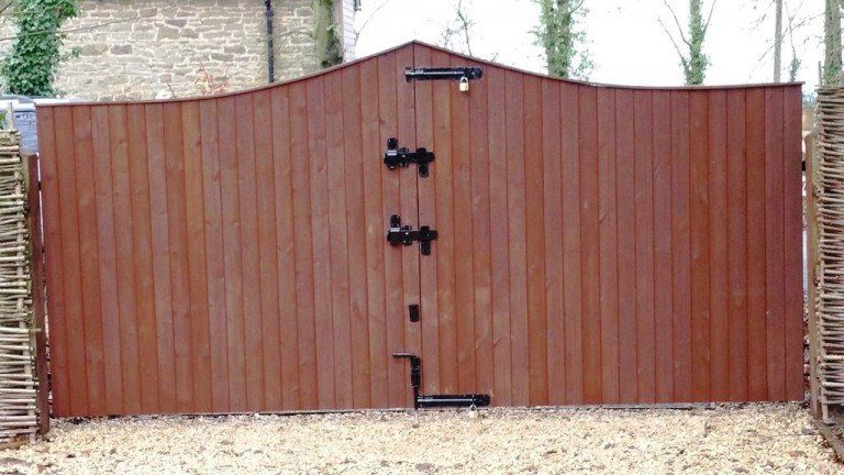 A wooden gate with a black handle is sitting on top of a gravel driveway.