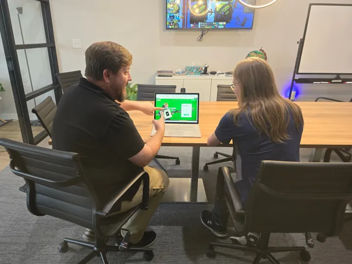Two people seated at a table, collaborating on a laptop in a bright meeting room.