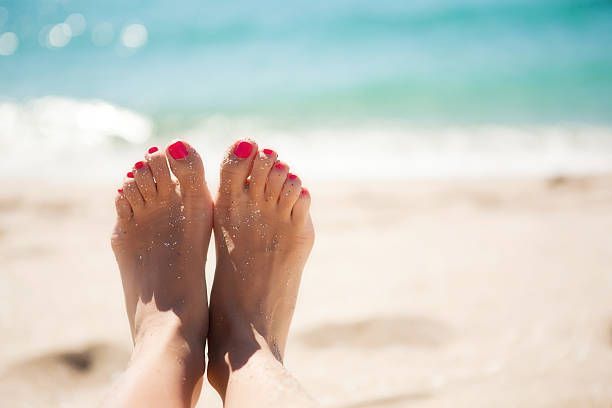 Feet with pink toenails resting on a sandy beach near turquoise water. — Kingscliff Podiatry Laser Clinic in Kingscliff, Nsw