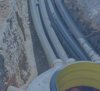Pipes in a trench, connected to a circular yellow-lined structure. Construction scene with brown soil.