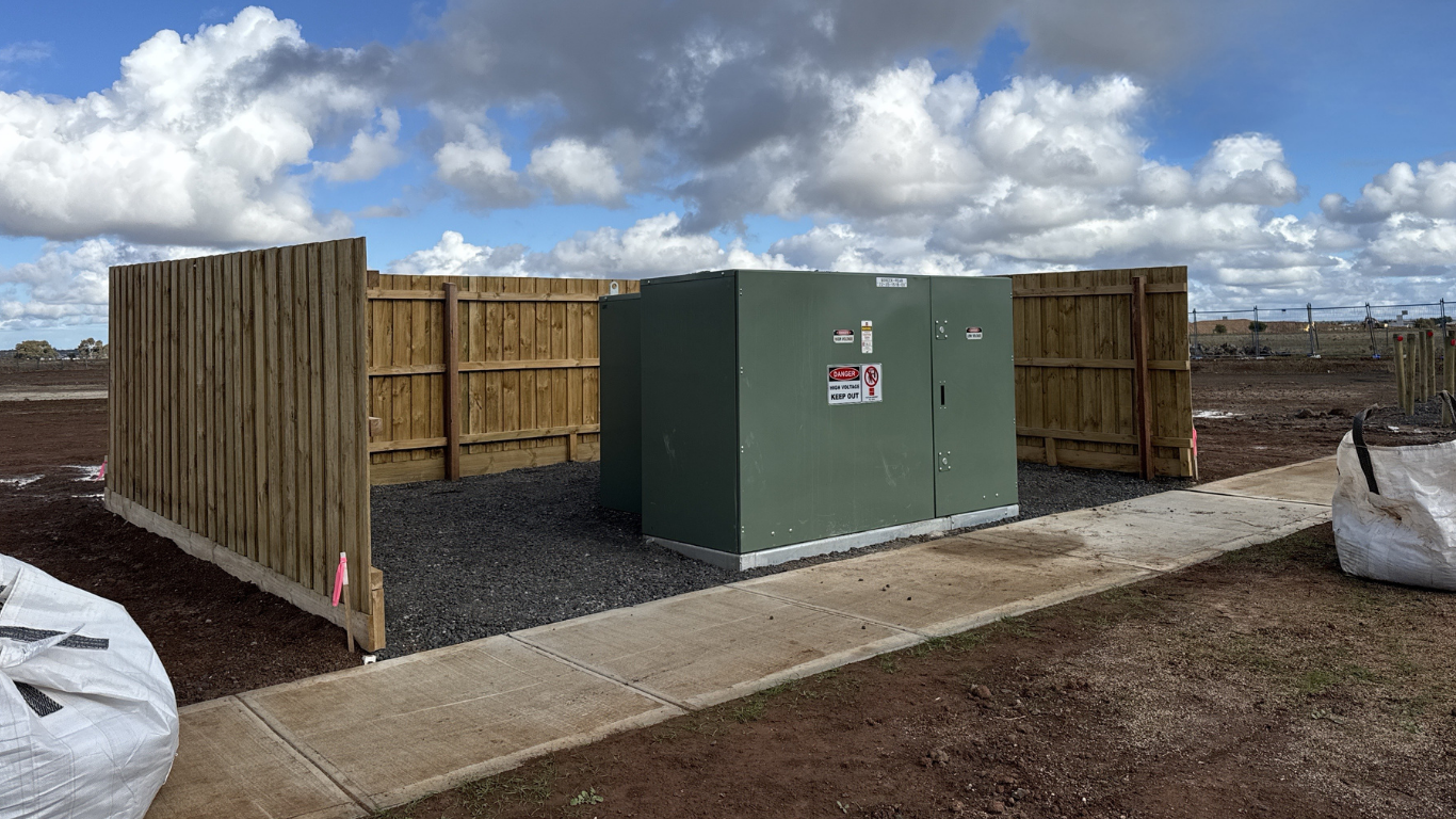 Utility enclosure on a concrete slab, with green metal cabinet and wooden fencing under a cloudy sky