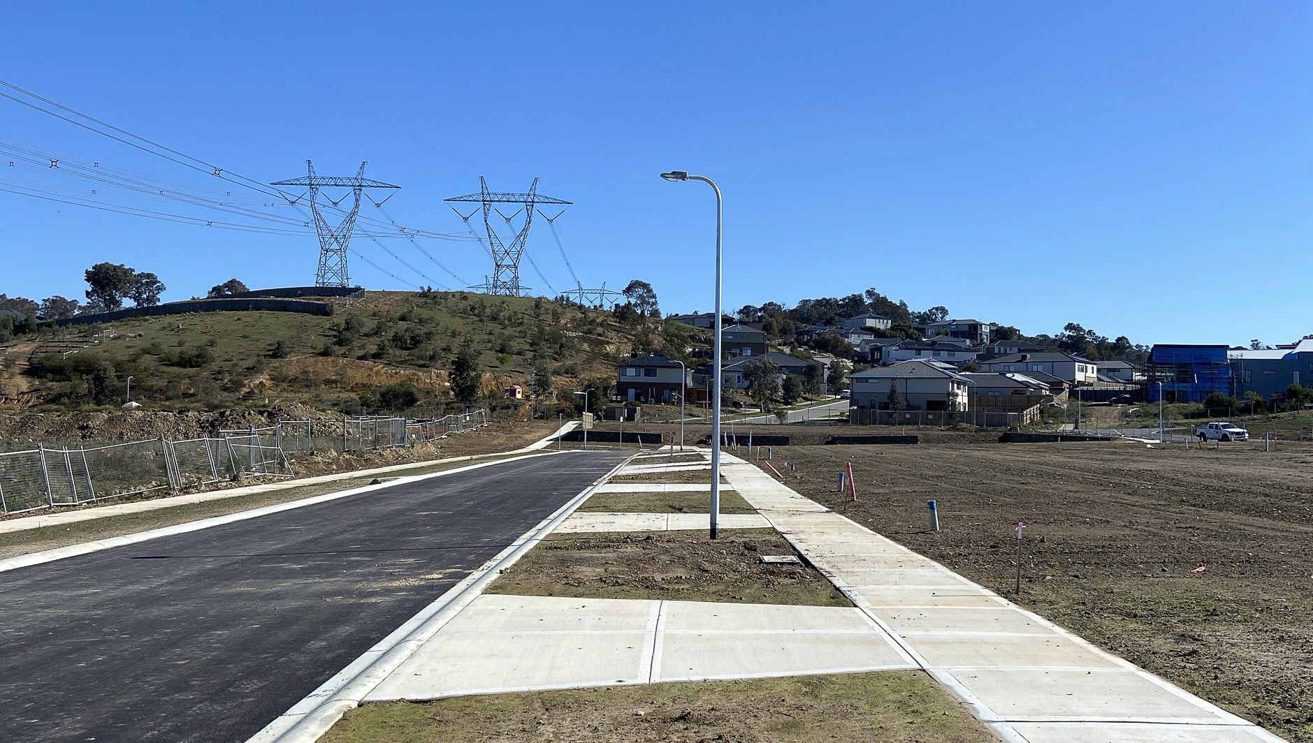 New sidewalk and road beside a grassy hillside under a clear blue sky