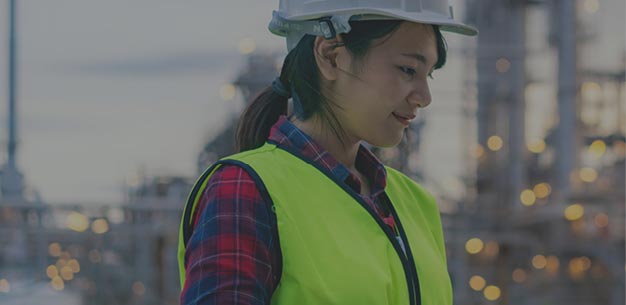 Woman wearing a hard hat and safety vest in an industrial setting.