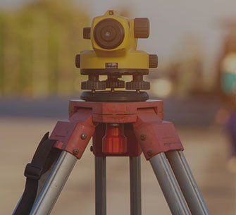Yellow and black surveying level mounted on a red and silver tripod outdoors.