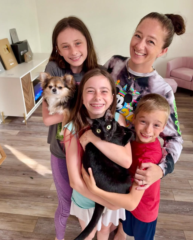 A group of four smiling people holding a small dog and a black cat in a bright, modern room.
