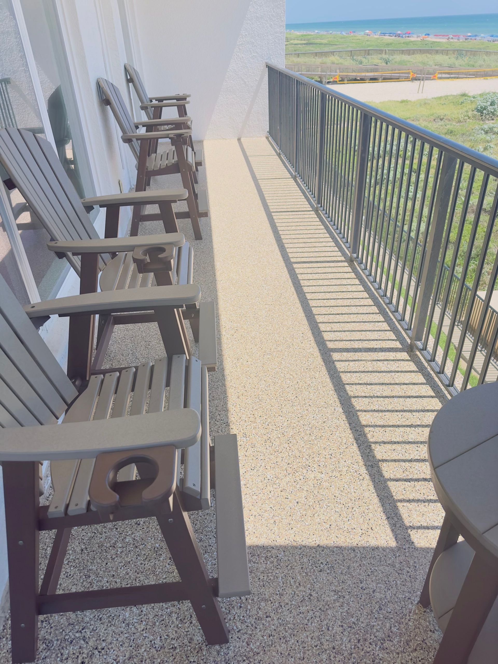 Outdoor seating on a balcony overlooking the ocean with gray chairs and a metal railing.
