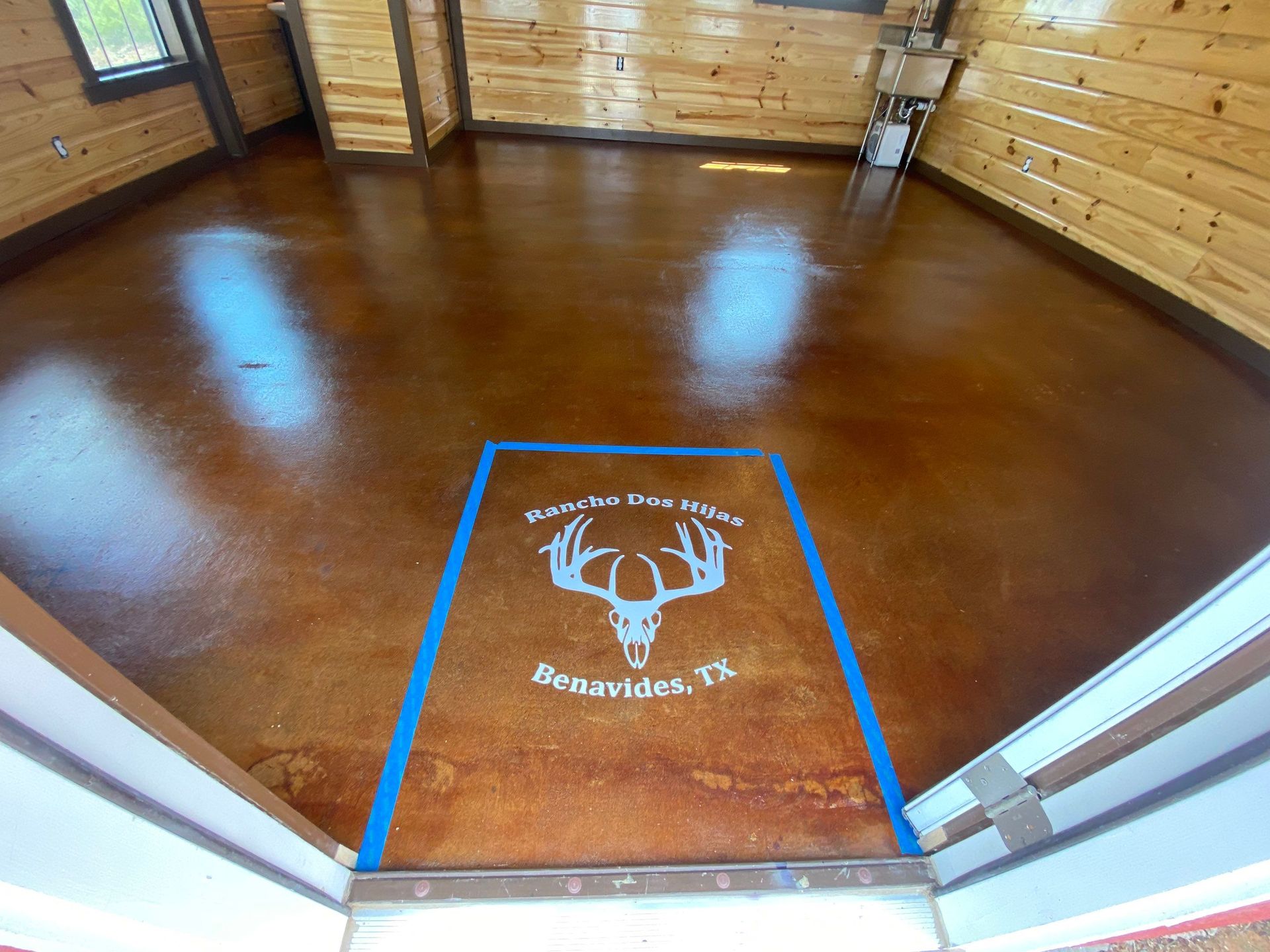 Room with brown concrete floor and wooden walls, a blue-bordered mat with a deer skull logo.