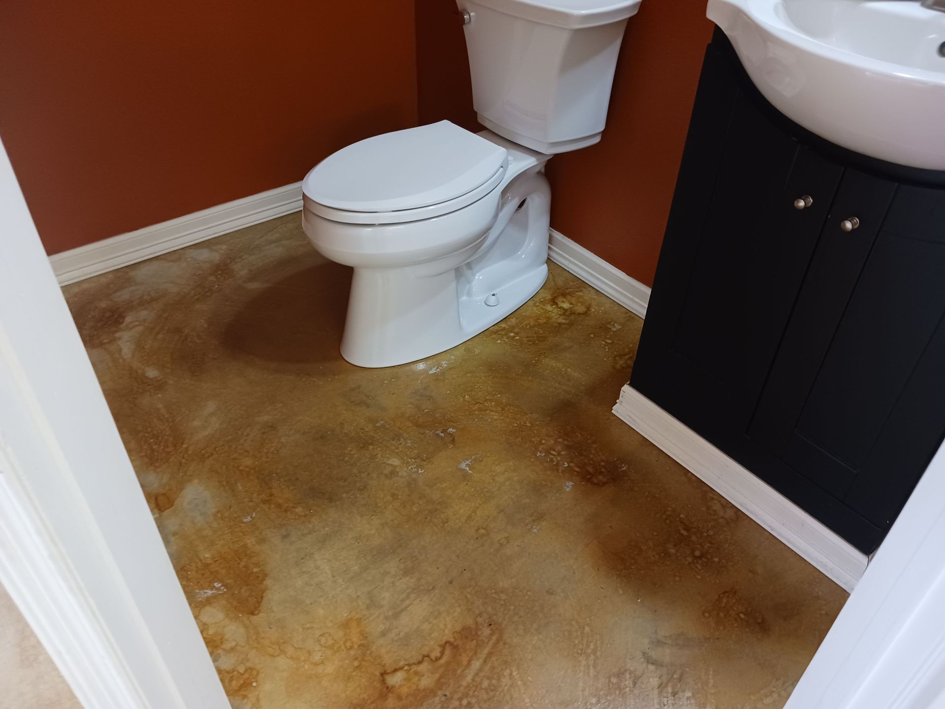 Small bathroom with a white toilet, black vanity, and stained brown floor.