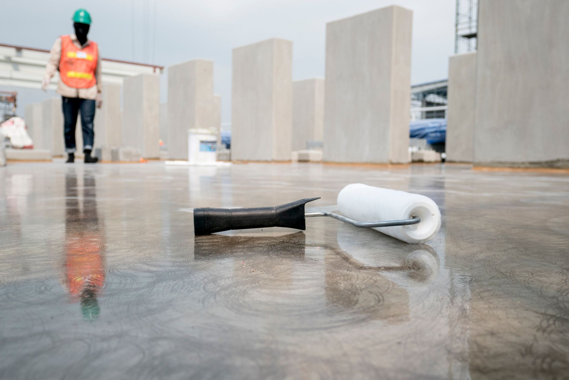 Worker using a roller to paint concrete, illustrating the application of commercial epoxy flooring.