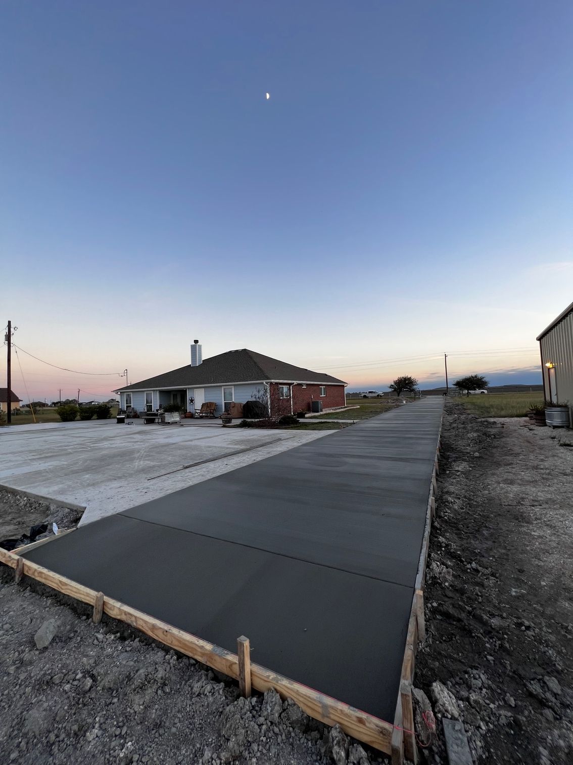 New concrete driveway construction, with a house in the background at dusk.