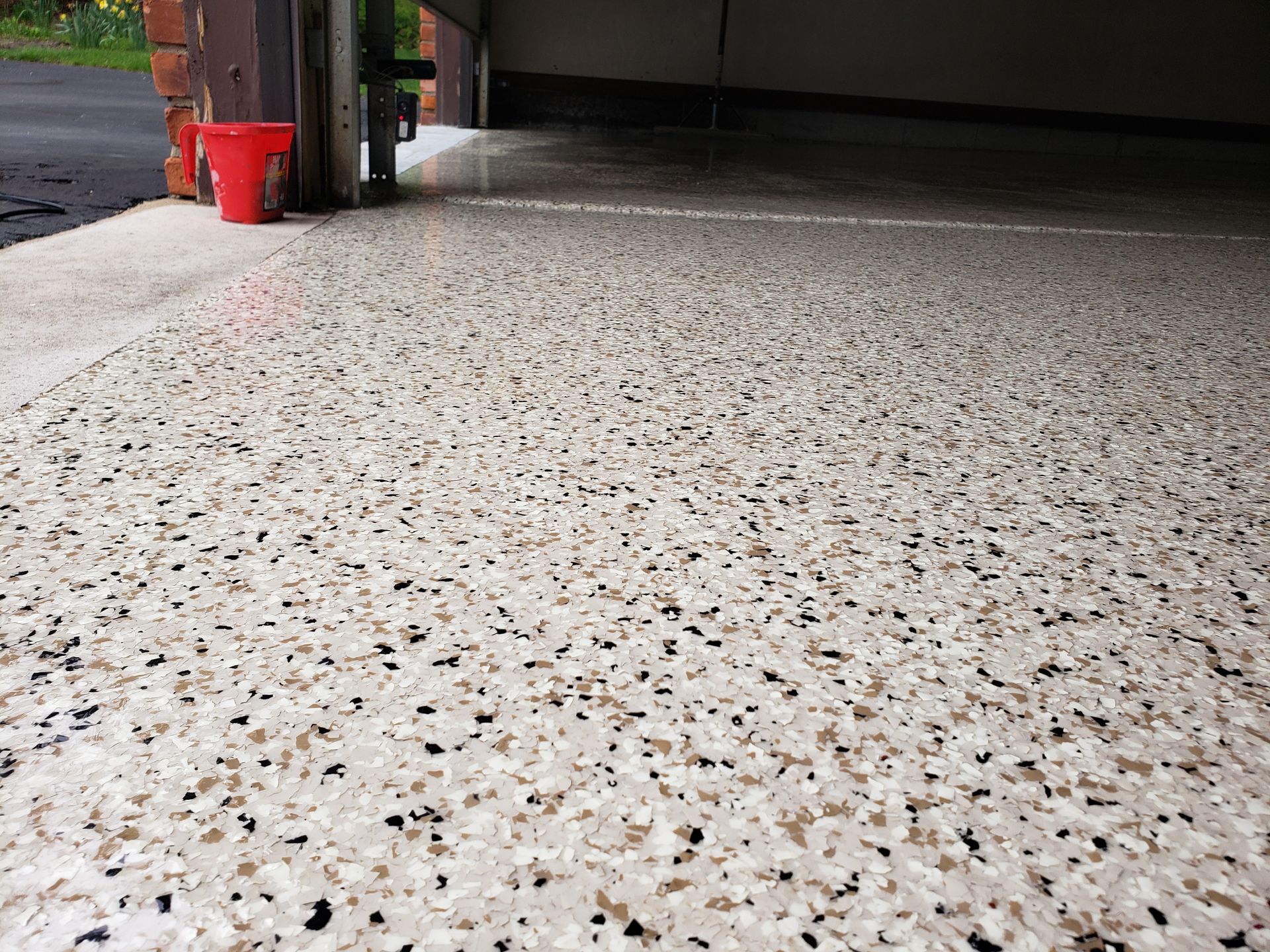 Speckled floor inside an open garage with a red bucket near the entrance.