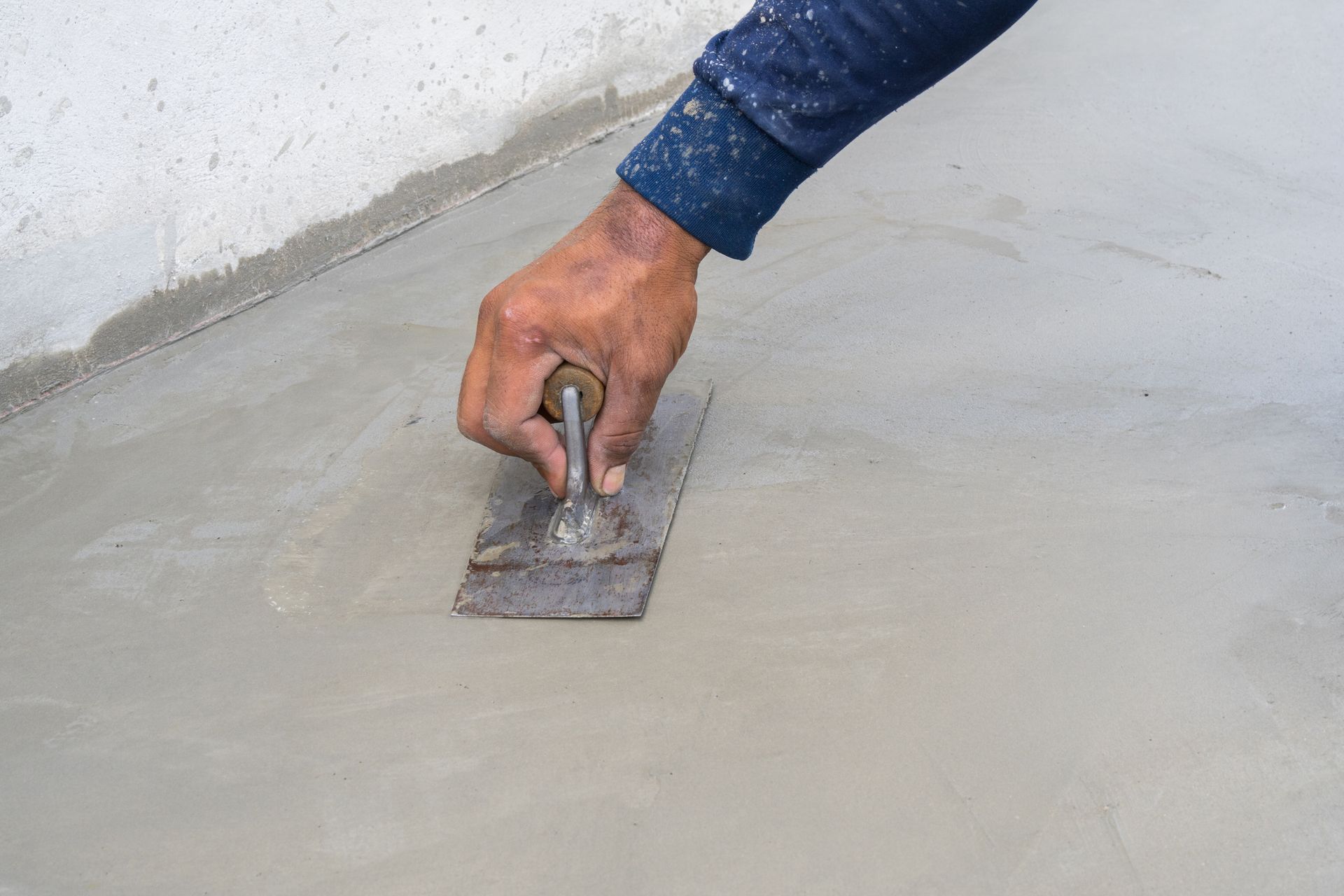 Hand using trowel to smooth freshly applied concrete during surface repair work.