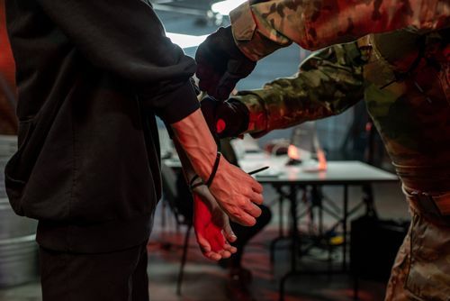 Officer in military outfit putting cuffs on hands of captured criminal