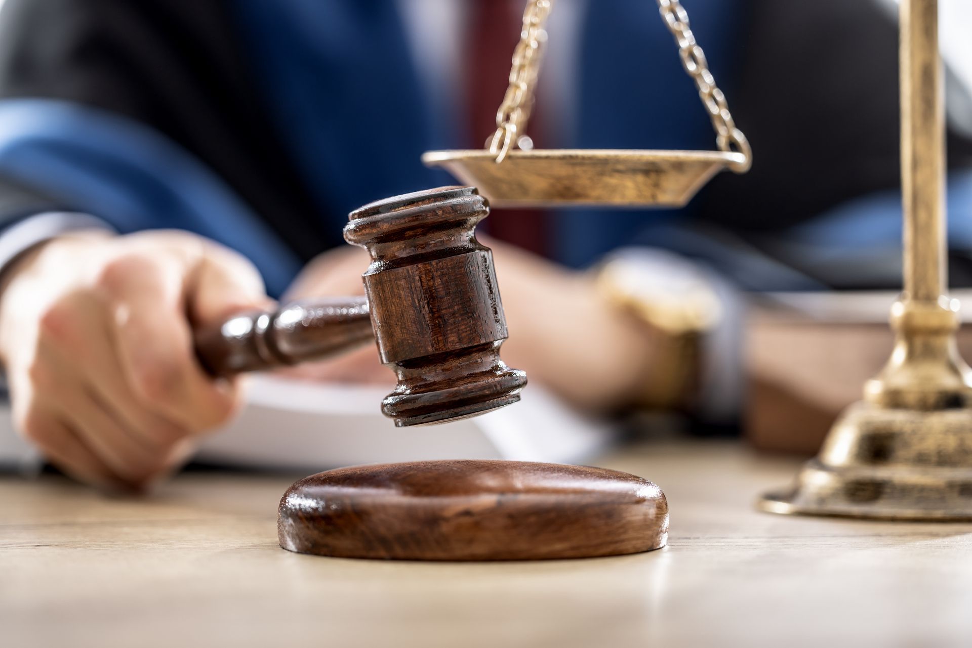 A judge is holding a wooden gavel in front of a scale of justice.