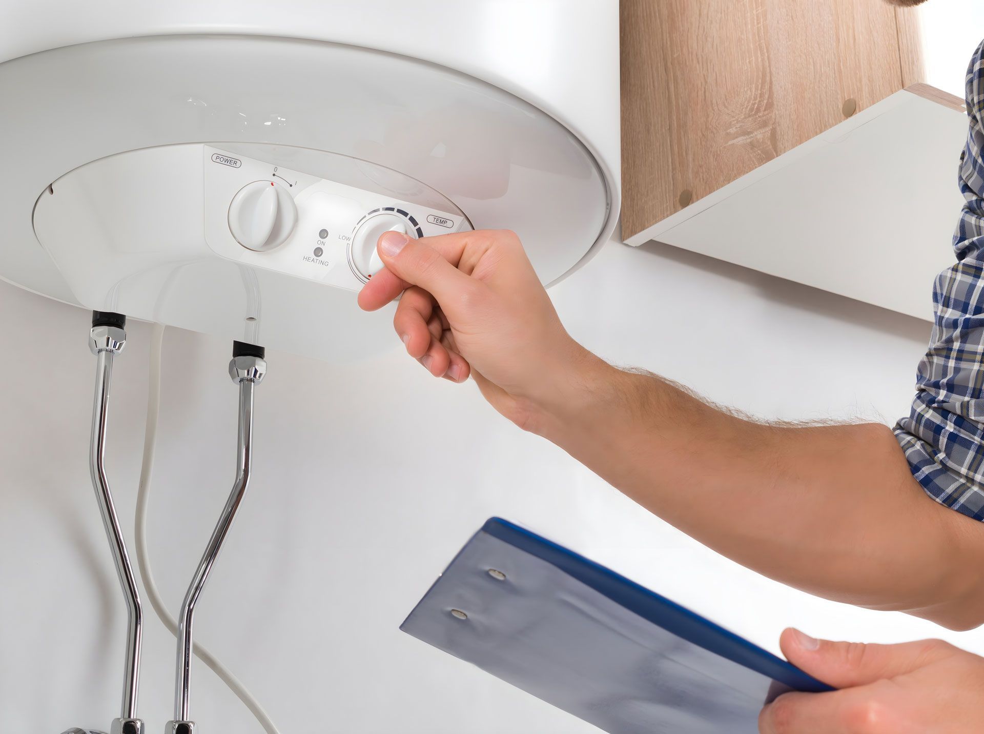 A man is adjusting a water heater while holding a clipboard.