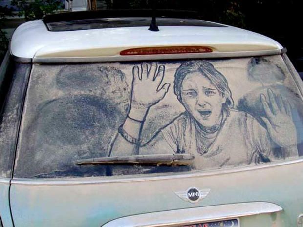 A dirty mini cooper with a drawing of a woman waving on the windshield
