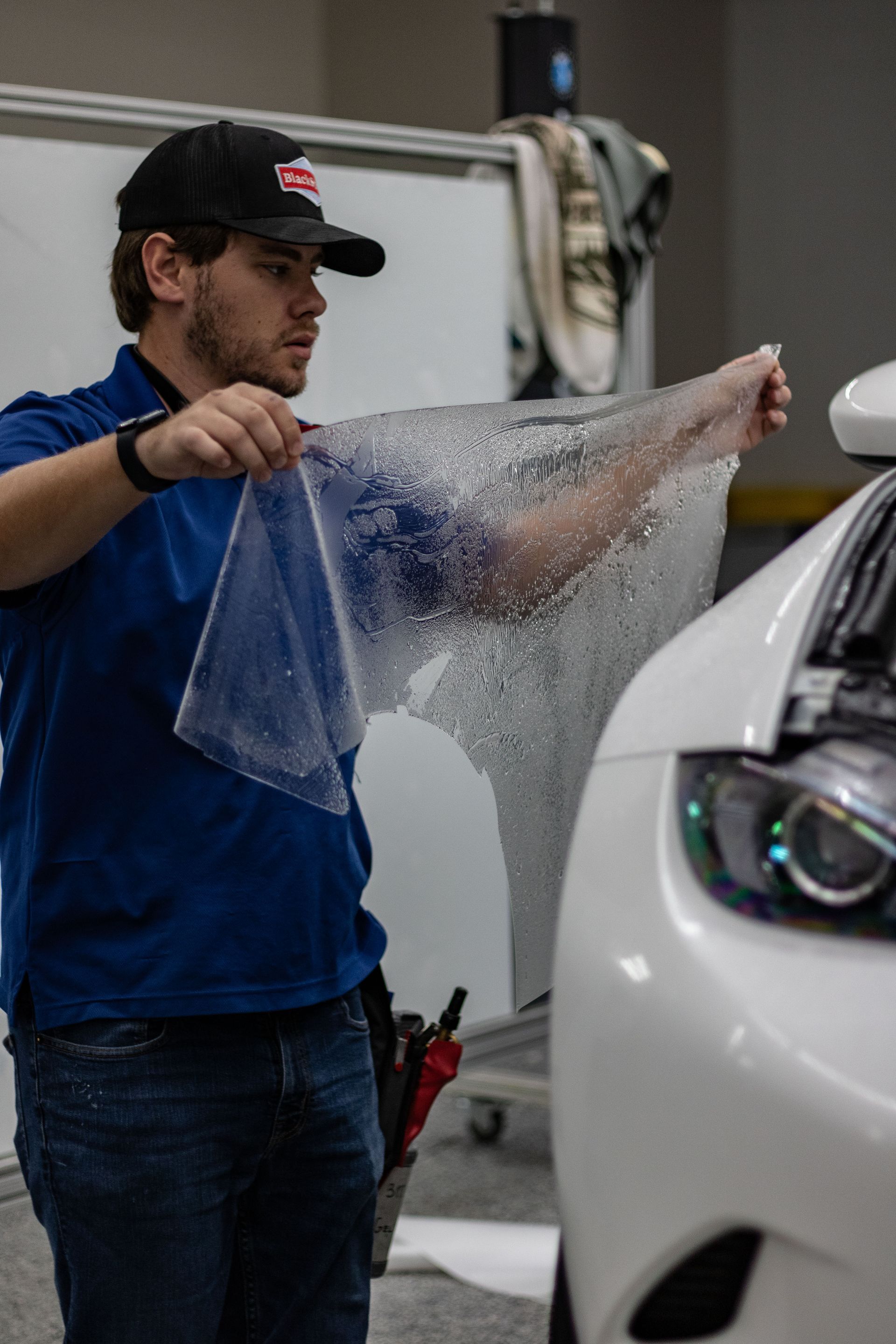 A man is wrapping a car with a plastic bag.