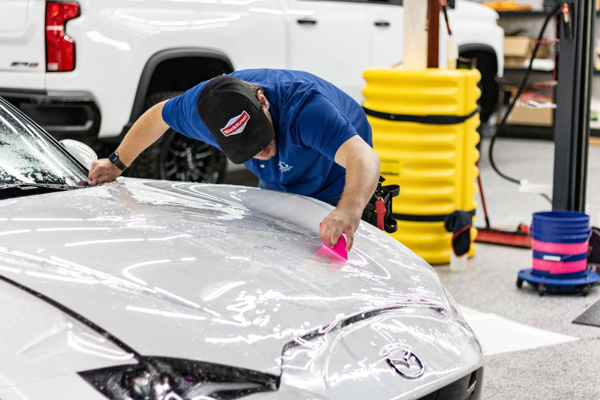 A man is wrapping a car with a plastic bag.