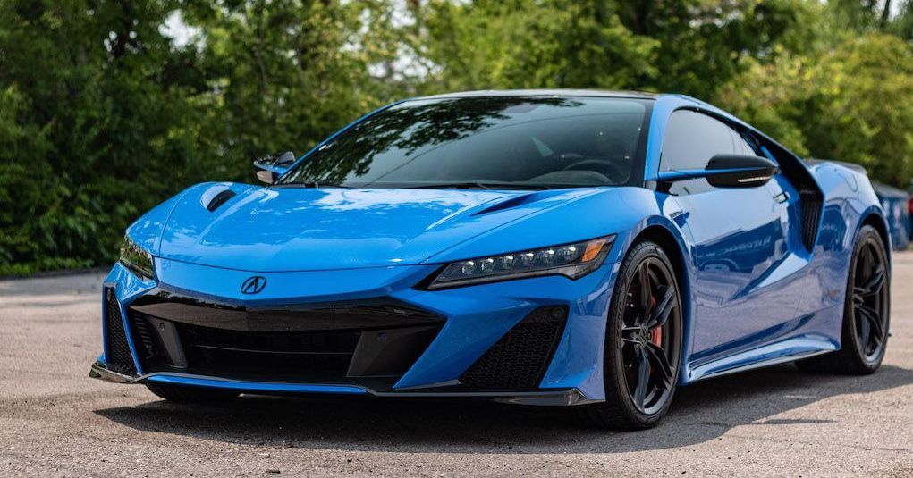 Blue Acura NSX sports car parked in front of green trees.