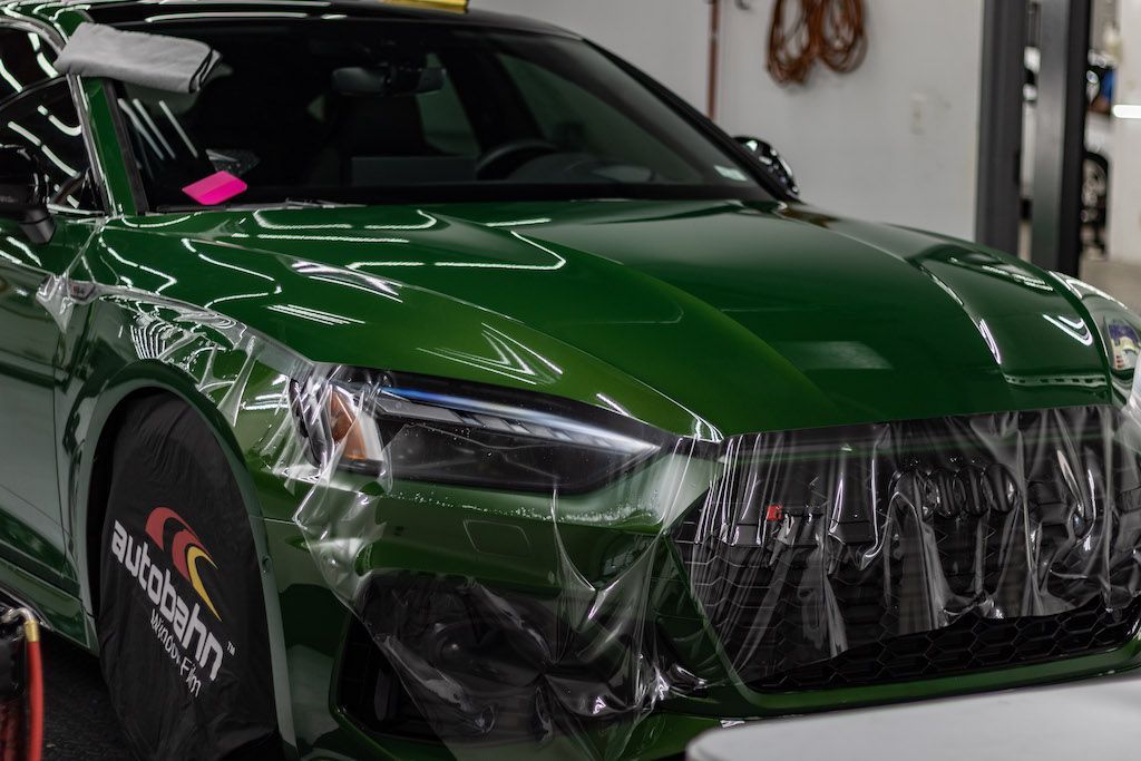 A green car is wrapped in plastic in a garage.