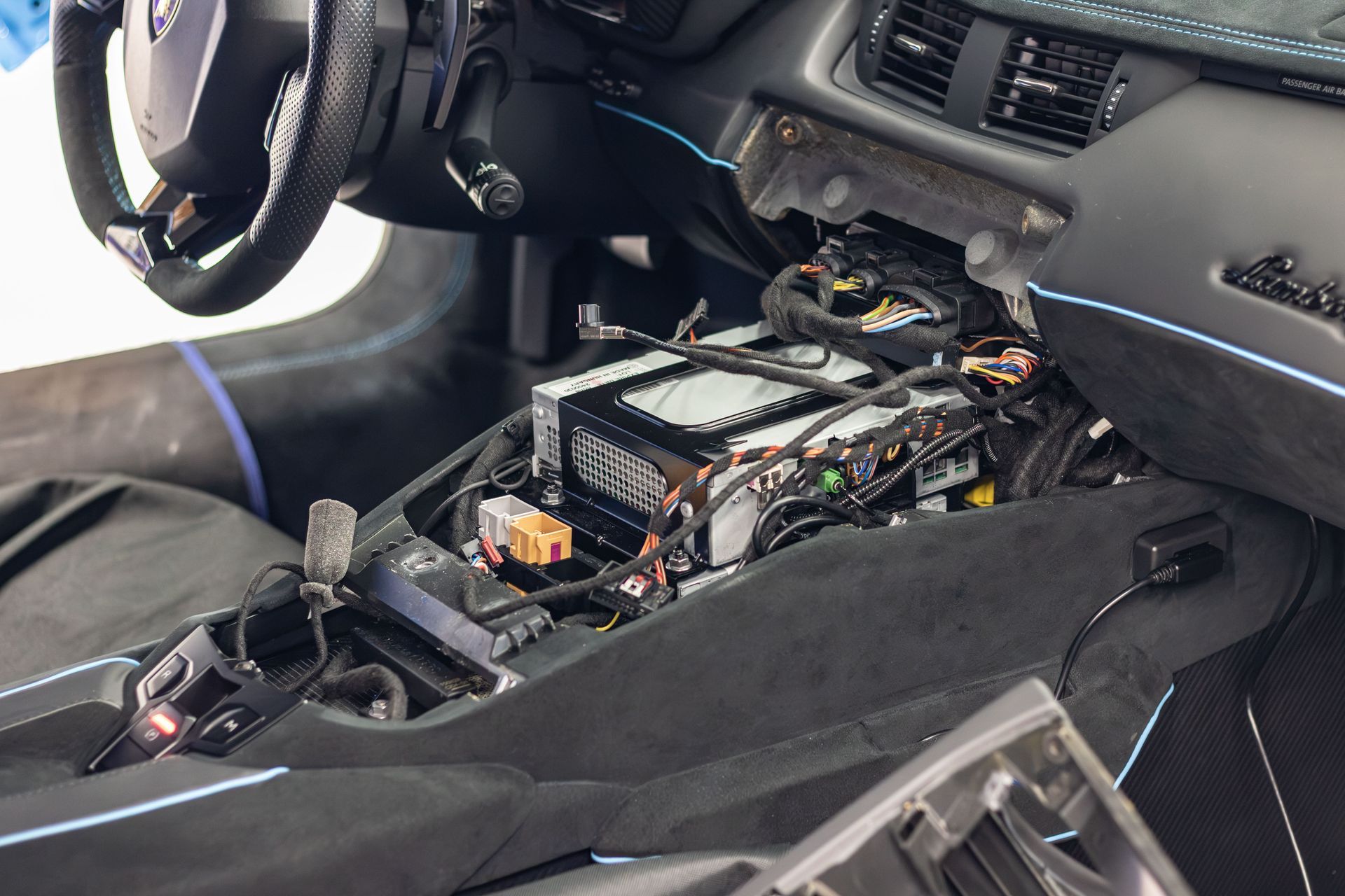 Car interior with center console removed, exposing electronic components and wiring under the dashboard.