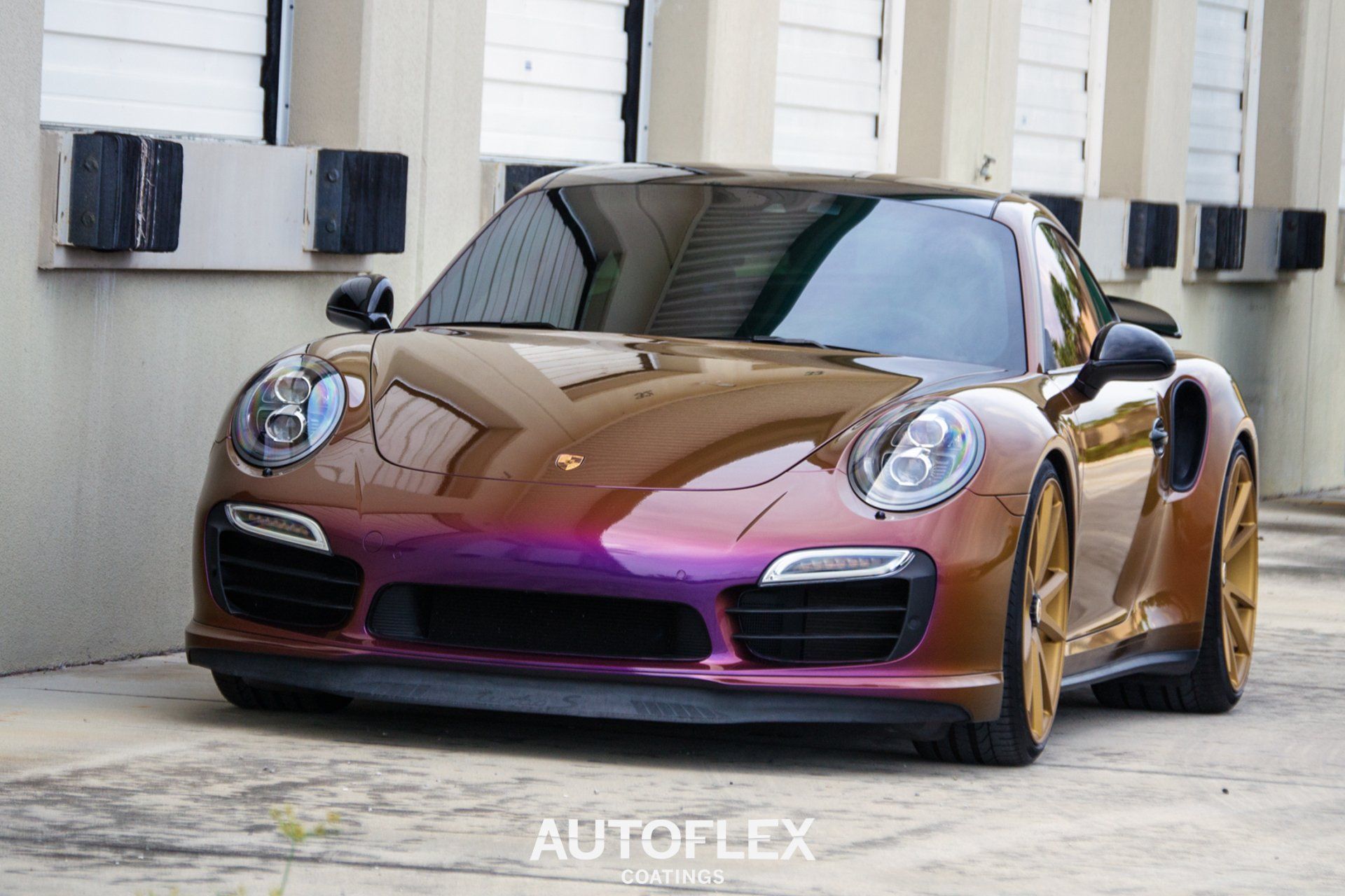 A porsche 911 turbo s is parked in front of a building.