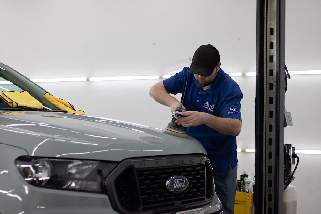 A man is polishing the hood of a car in a garage.