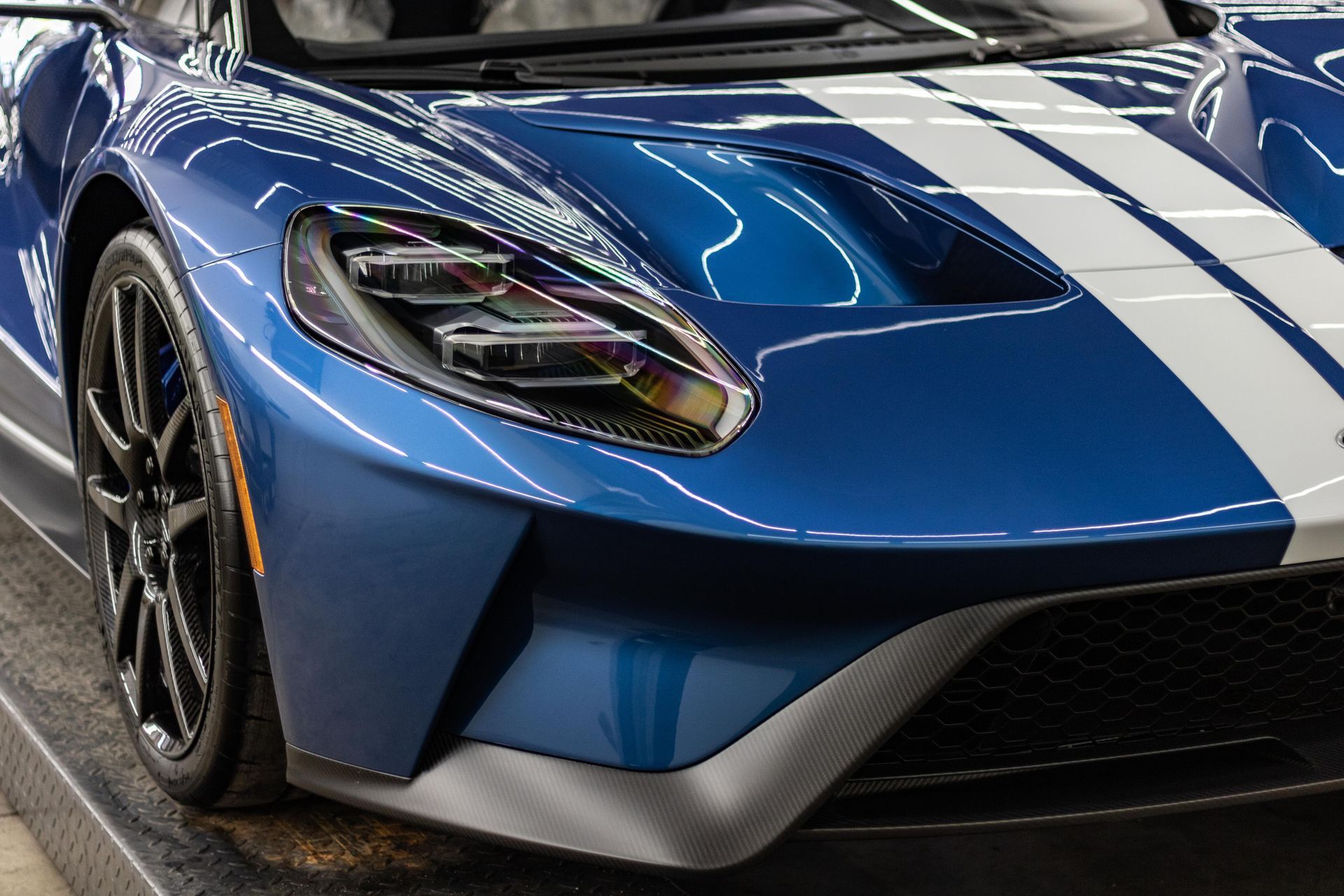 A blue sports car with white stripes is parked on a ramp.