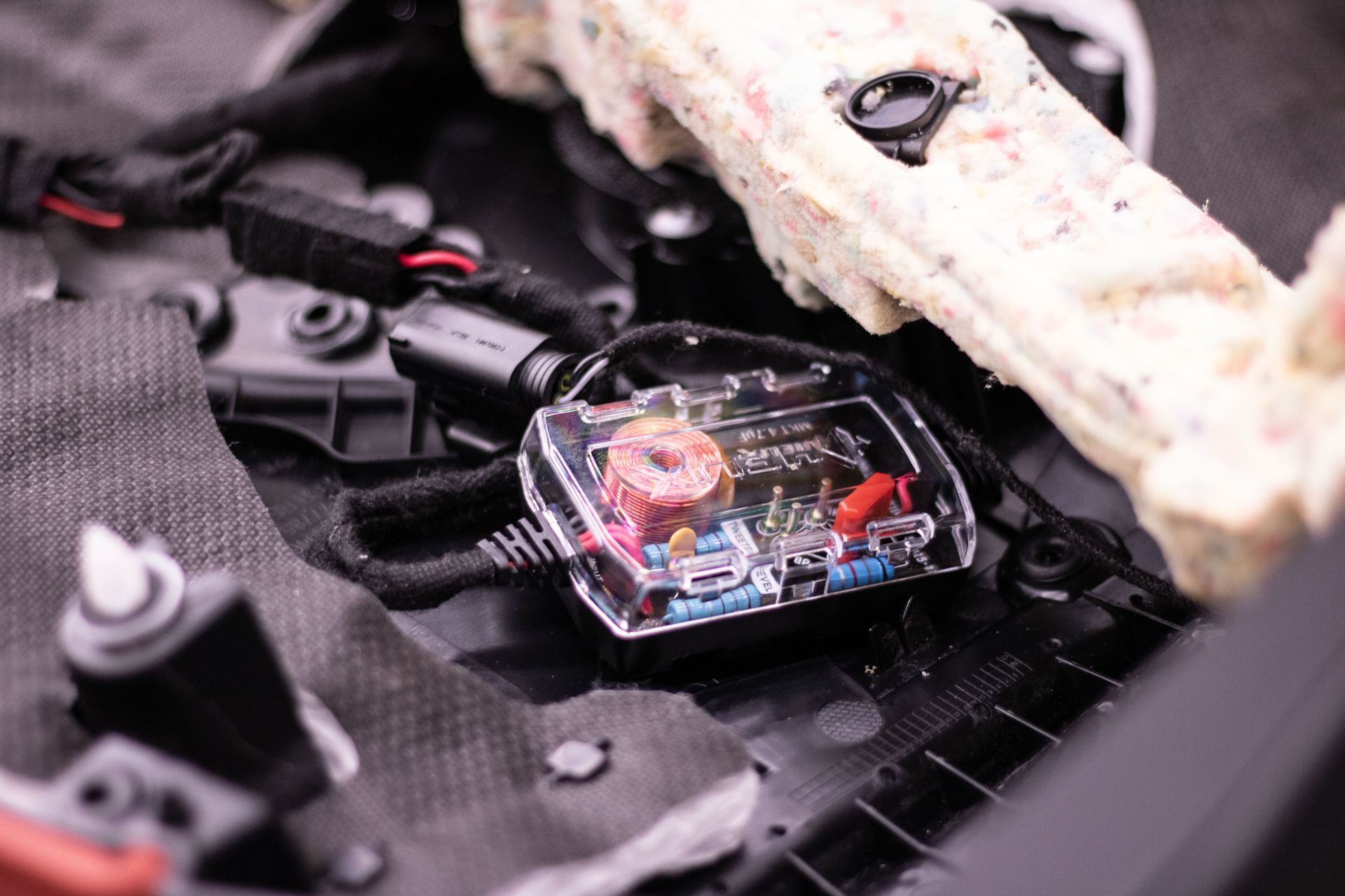 Clear plastic electronic component with colored wires mounted inside a vehicle engine bay