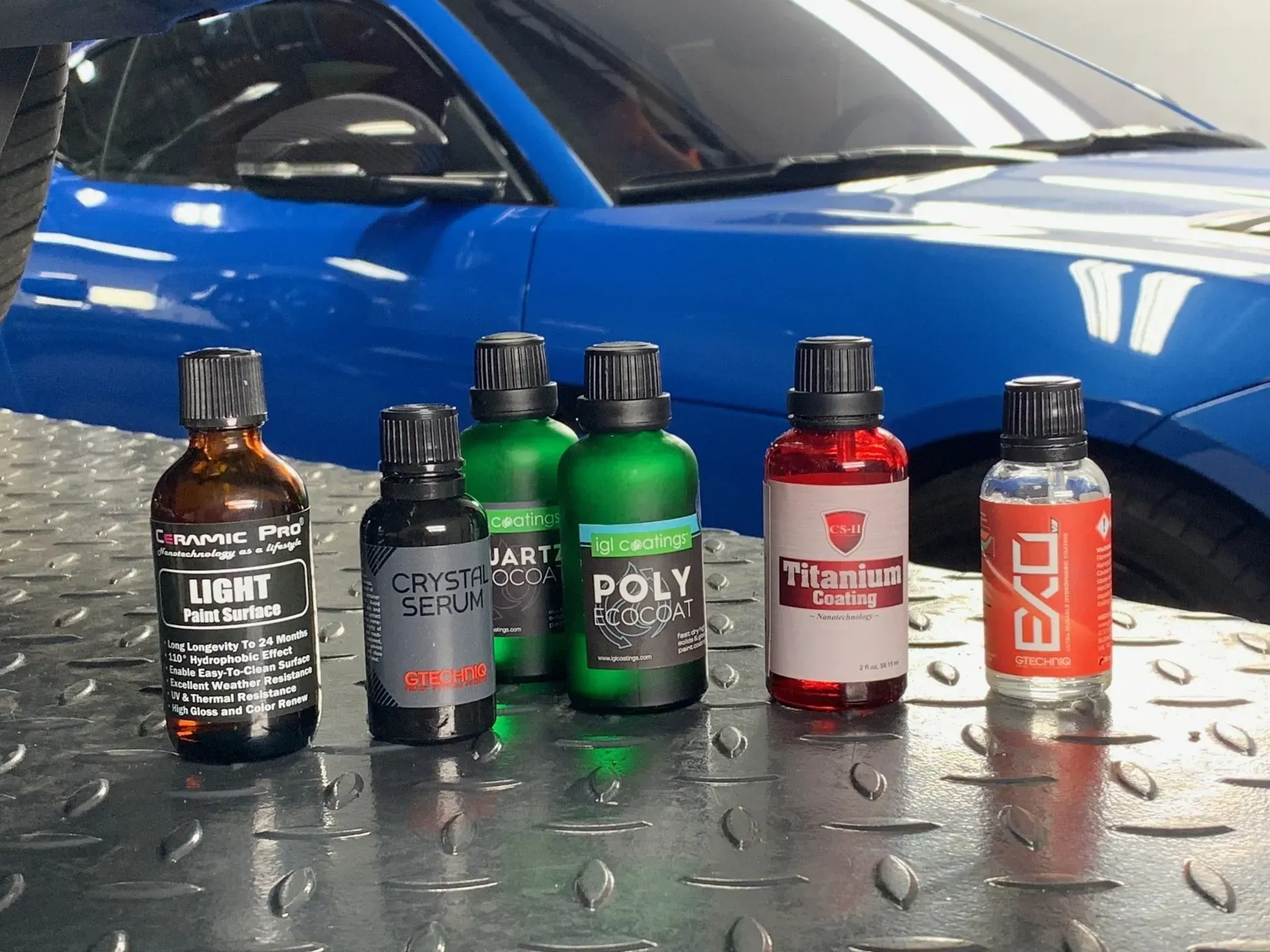 A group of bottles are sitting on a table in front of a blue car.