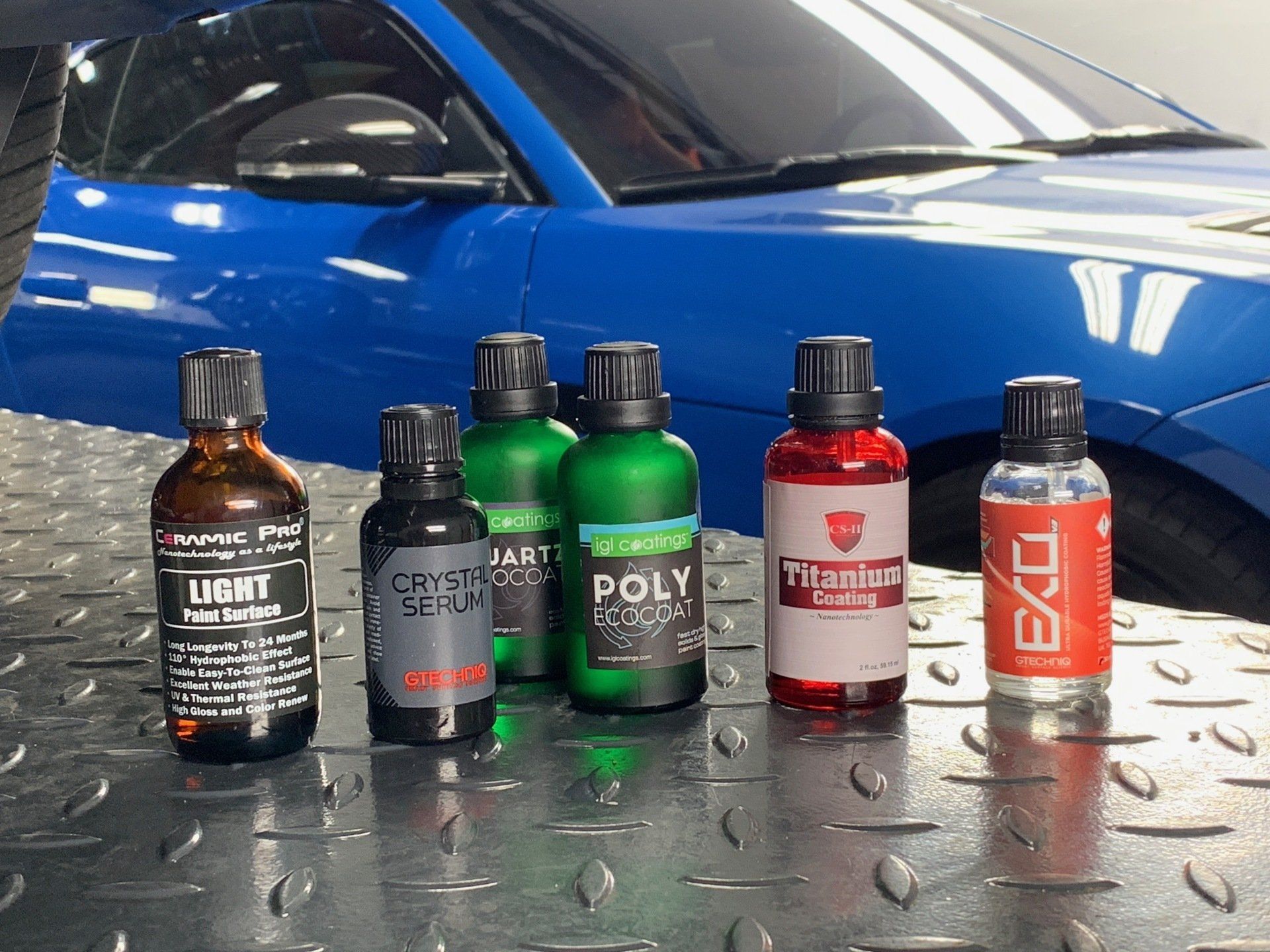 Several bottles of chemicals are lined up in front of a blue car