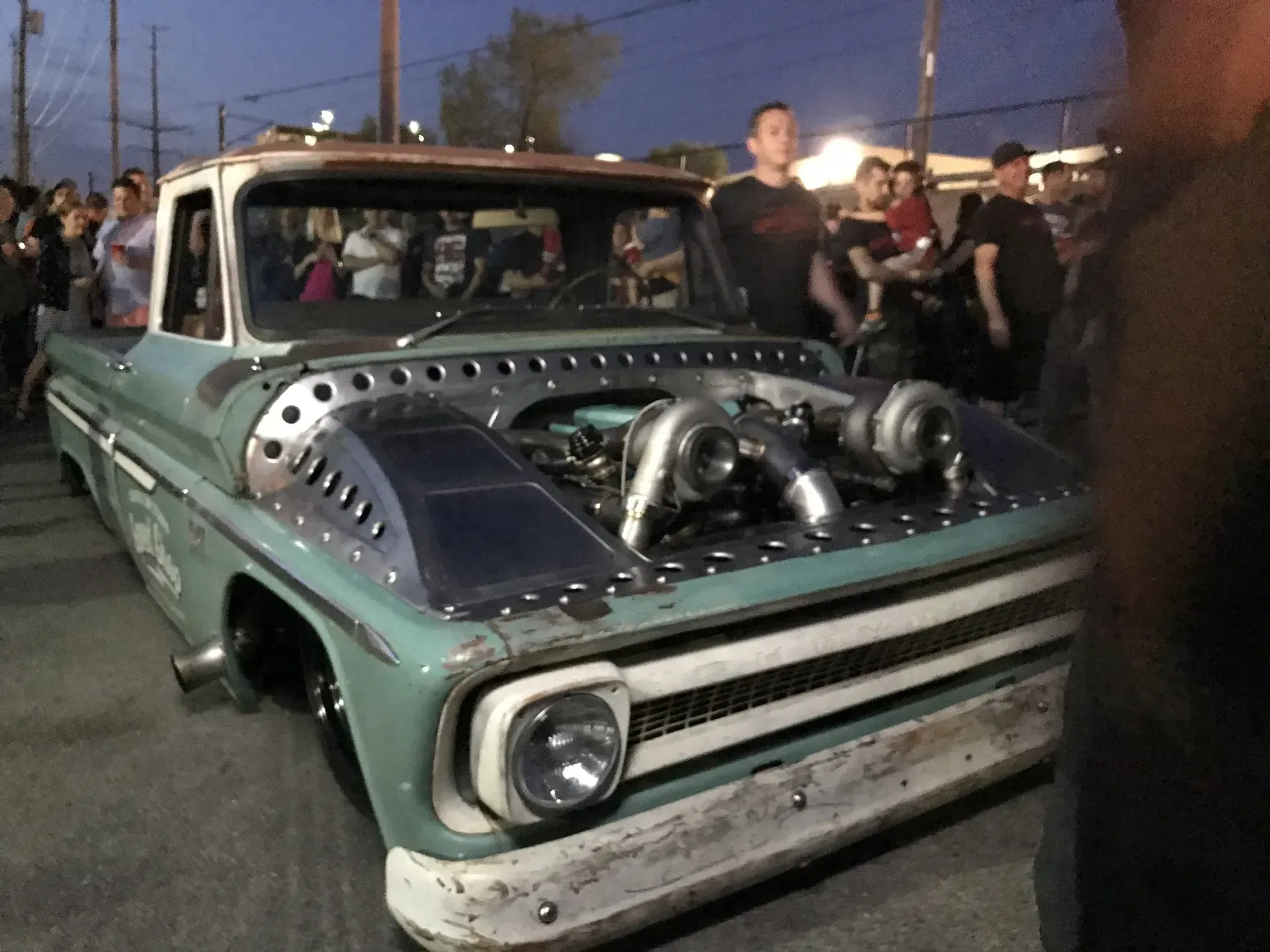 A group of people are standing around a truck with a turbo on the hood