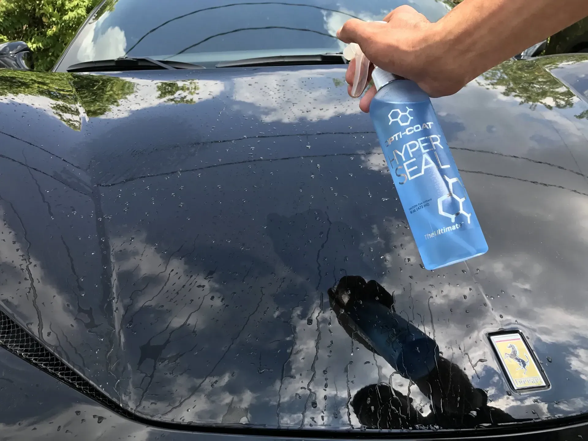 A person is spraying water on the hood of a car.