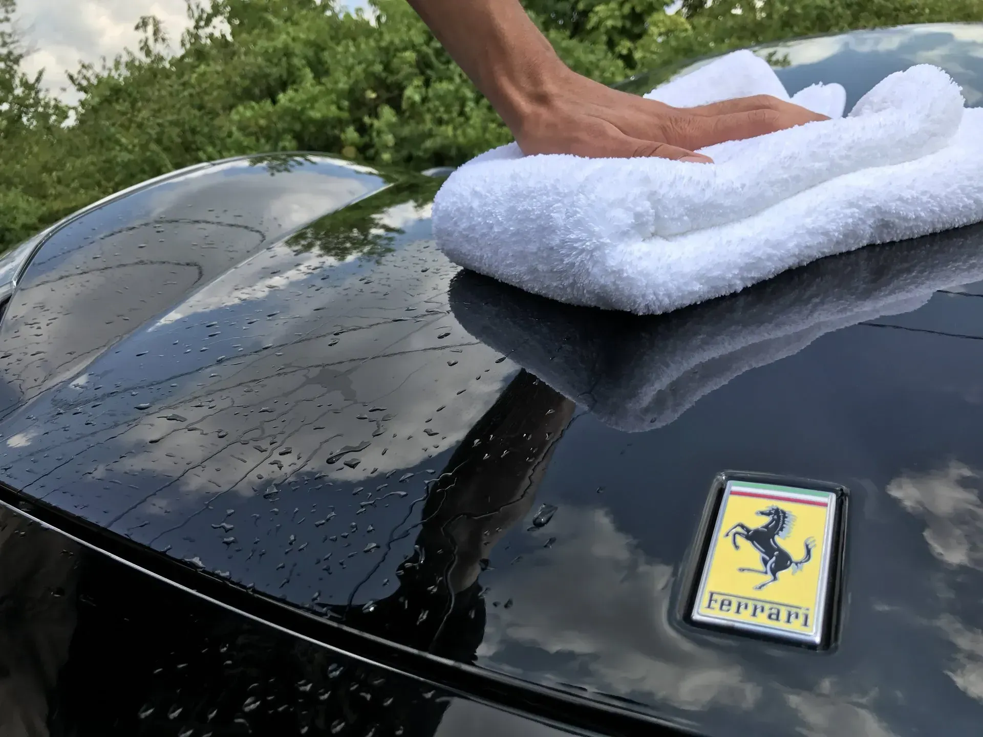 A person is cleaning a black ferrari with a towel