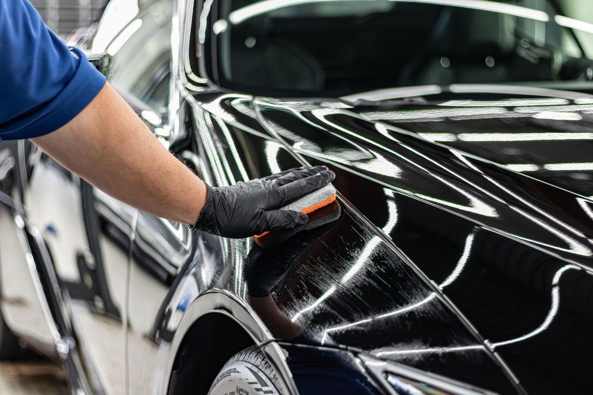 Person polishing a black car’s hood with a cloth in a detailing shop