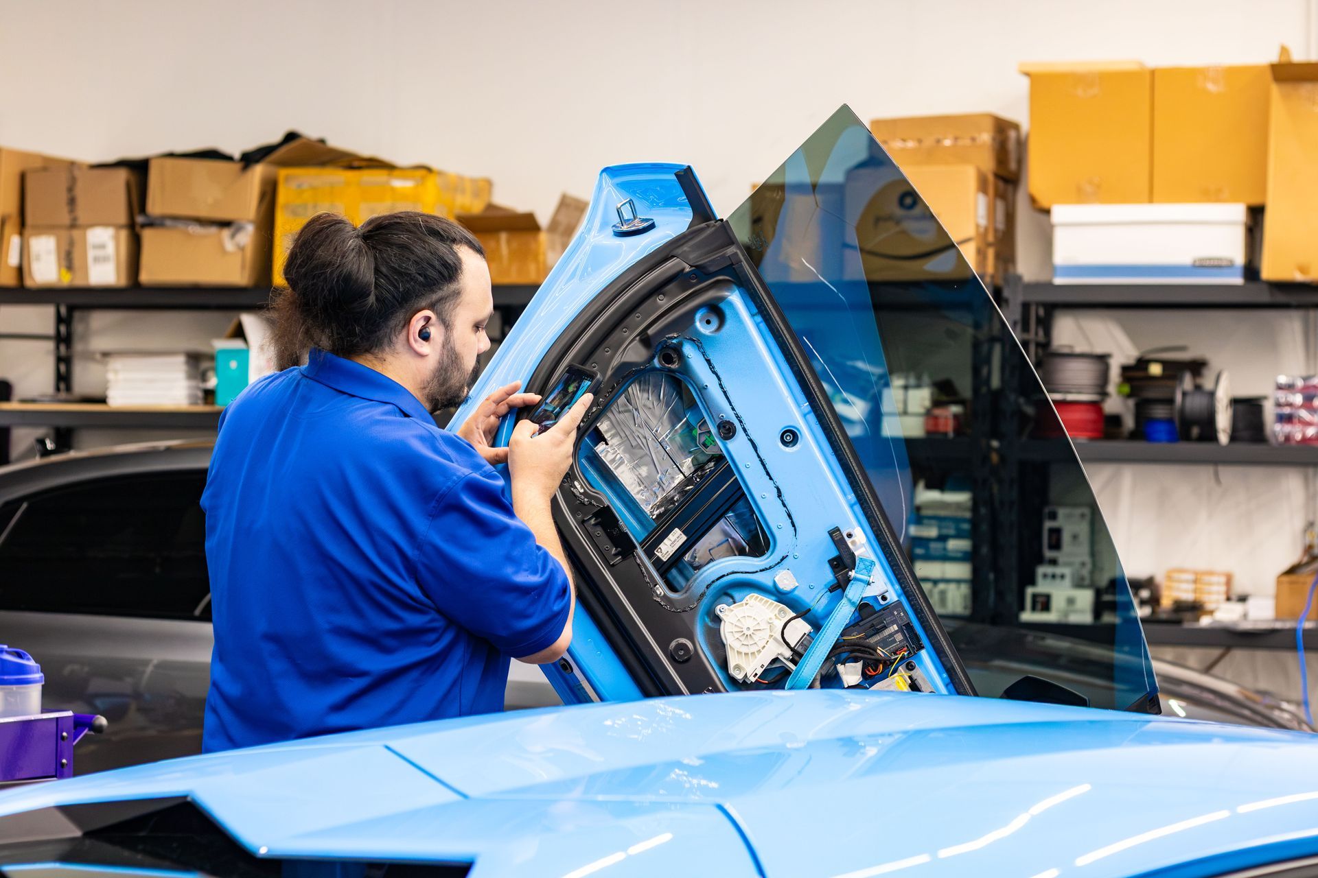 Mechanic working on a blue car door in an auto repair shop