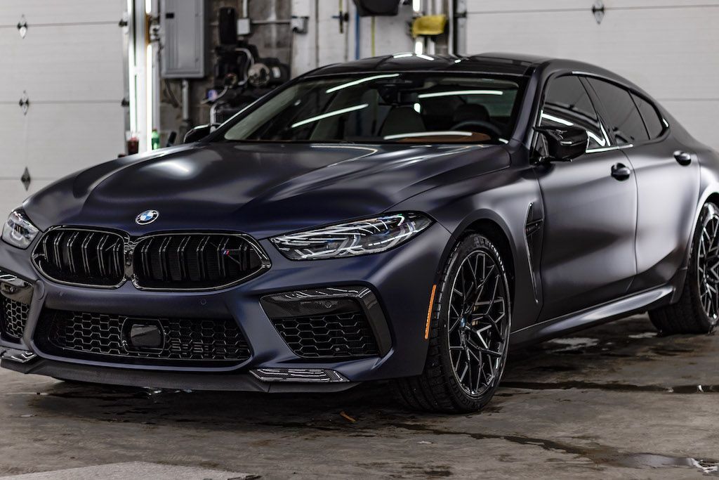 A black bmw m8 is parked in front of a garage door.
