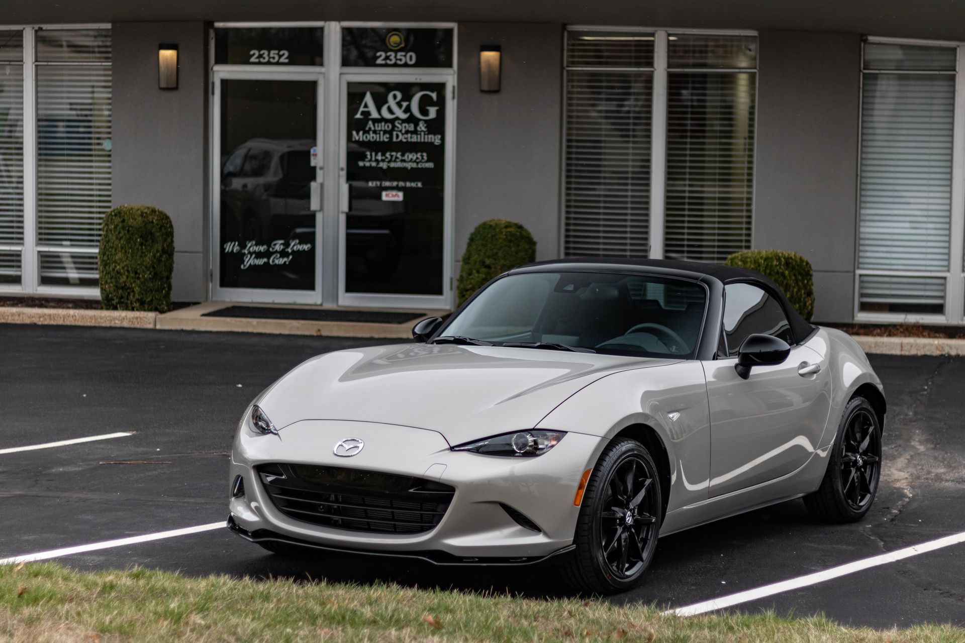A silver sports car is parked in a parking lot in front of a building.