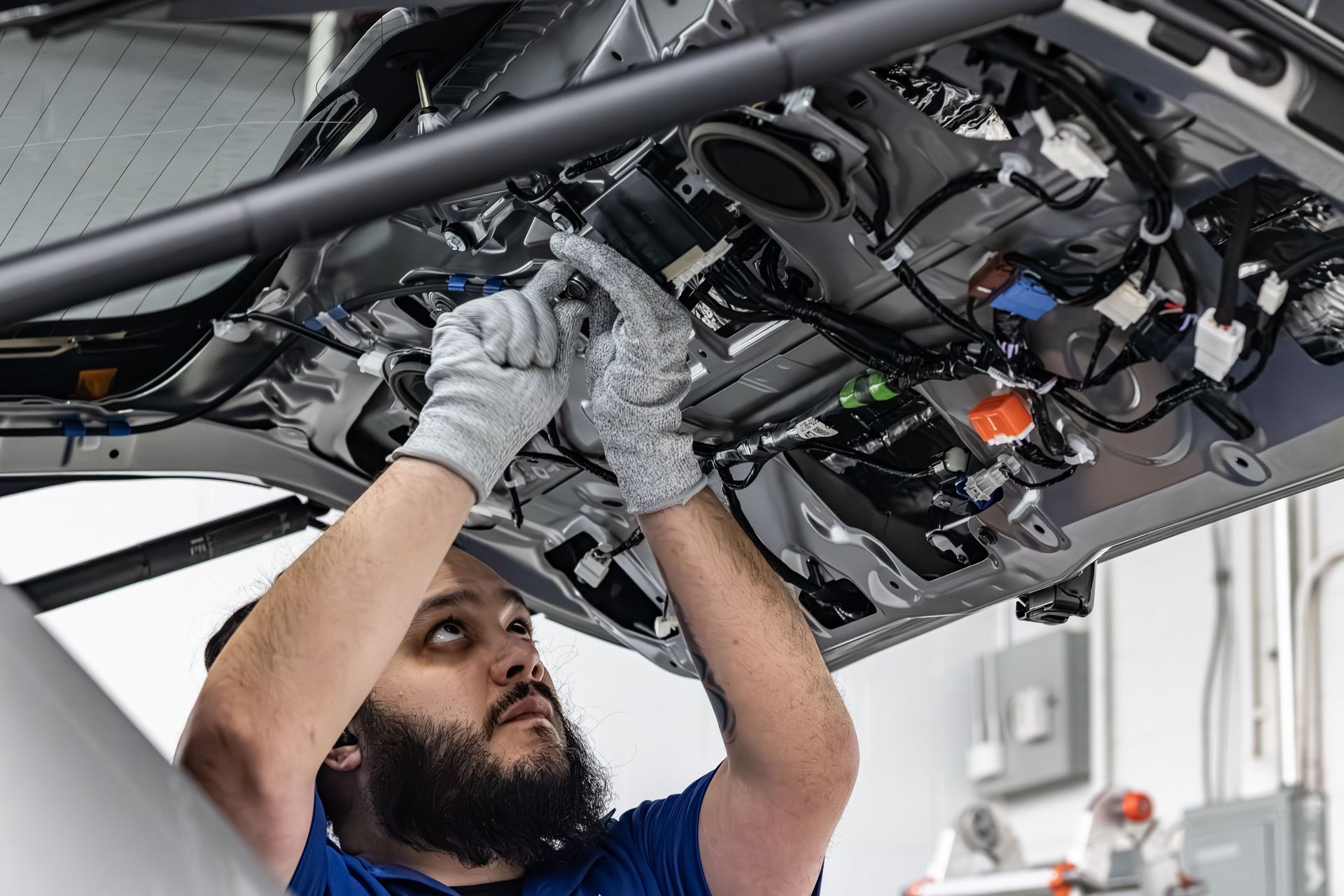 Mechanic working under a vehicle, inspecting wiring with gloves in an auto repair shop