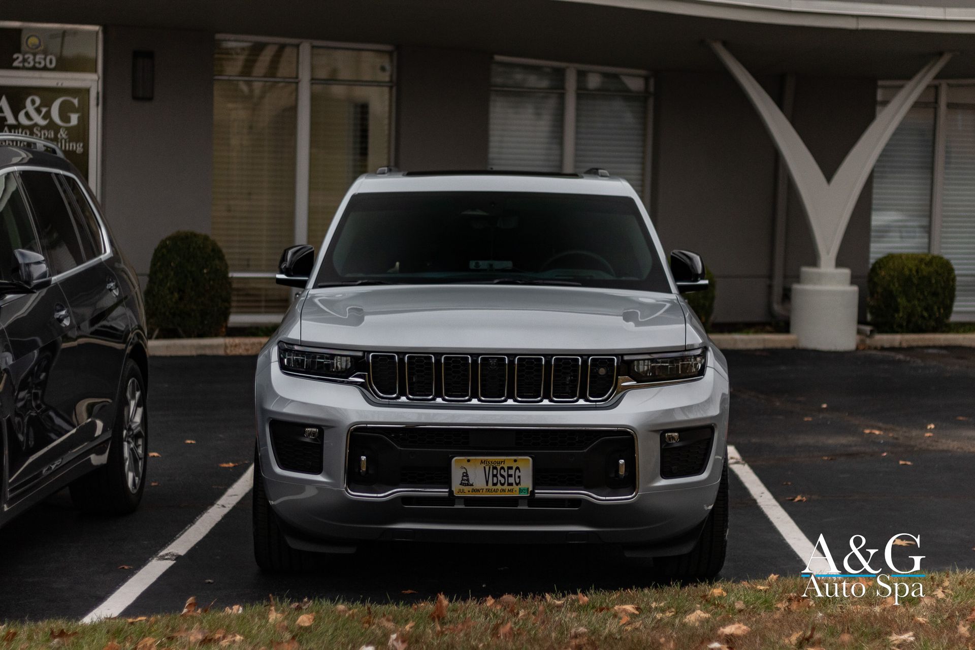 A silver jeep is parked in a parking lot in front of a building.