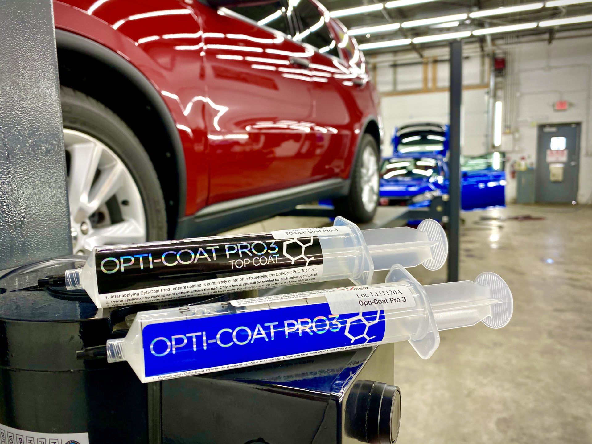 A red car is parked in a garage next to a stack of syringes that say opti-coat pro