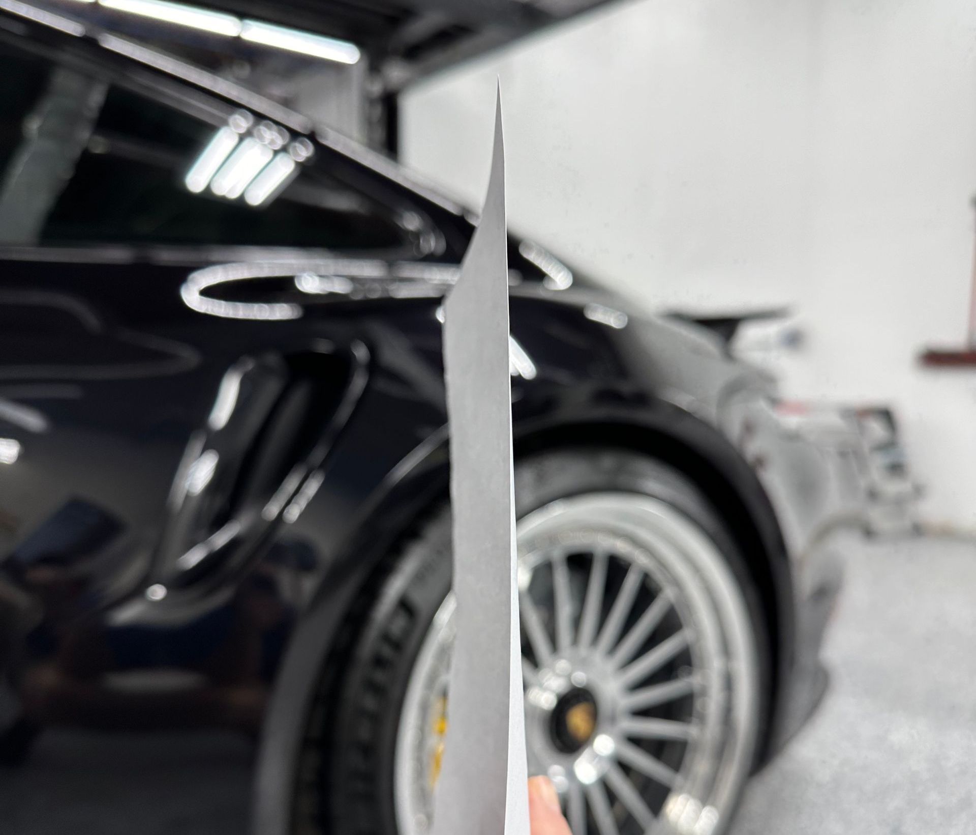 A person is holding a piece of paper in front of a car.