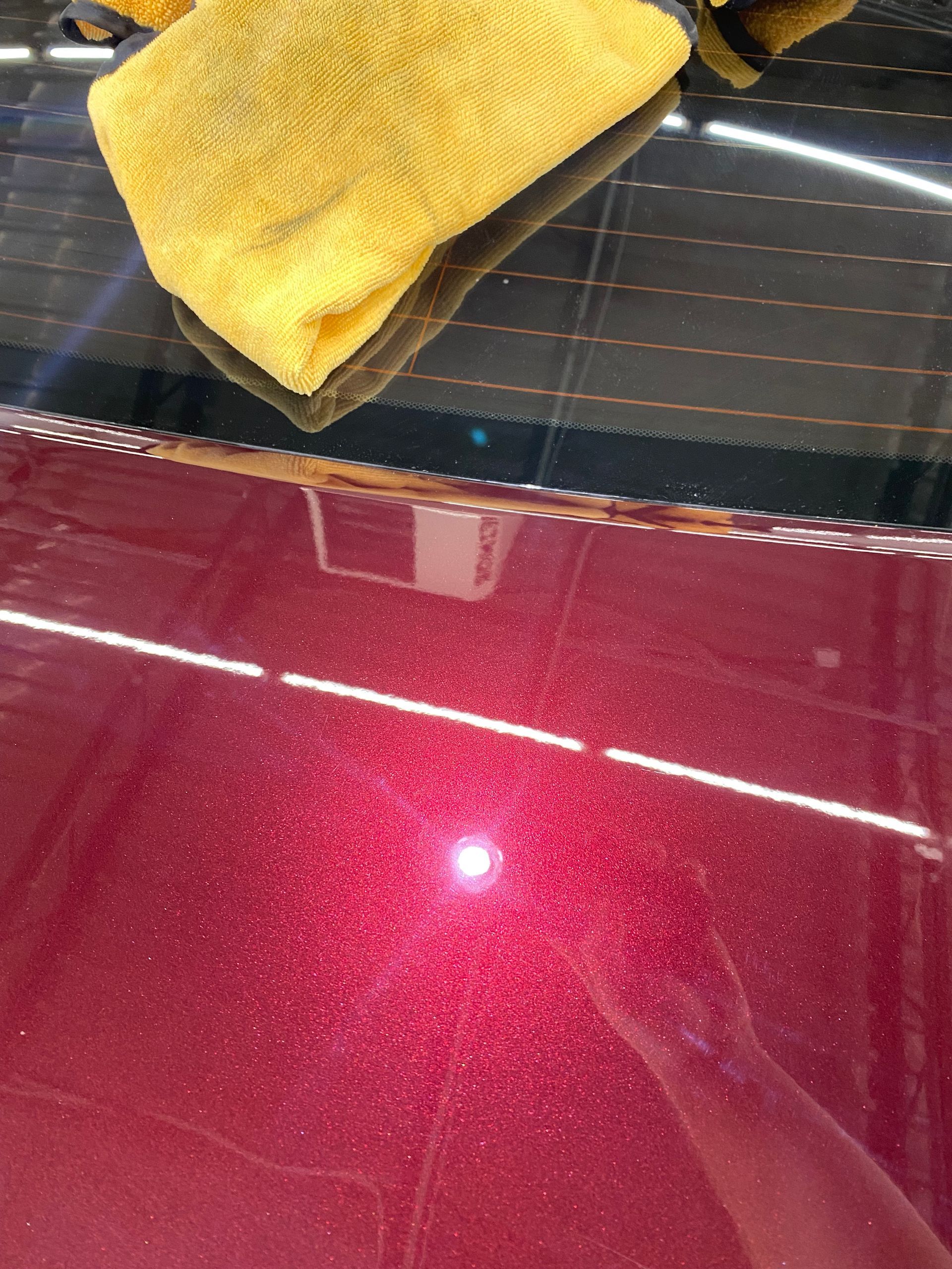 A person is cleaning a red car with a towel.