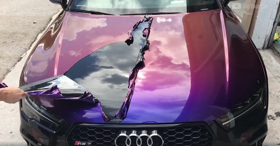 A person is peeling off the hood of a purple car.