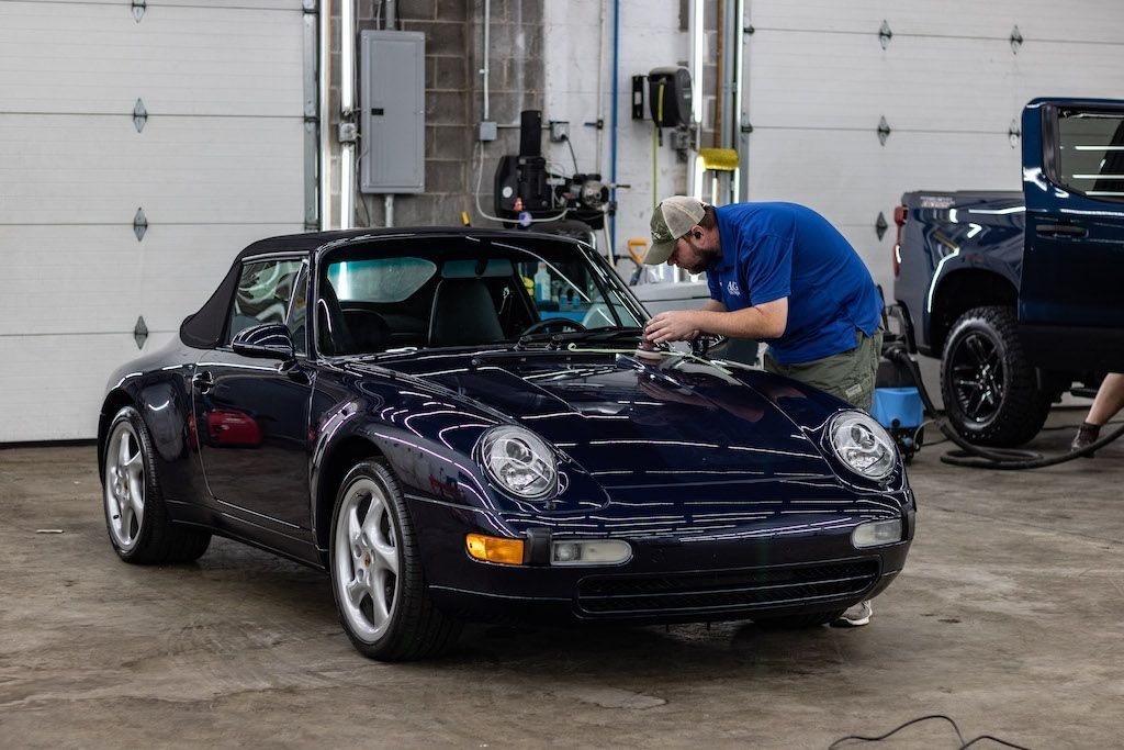 A man is working on a blue porsche in a garage.