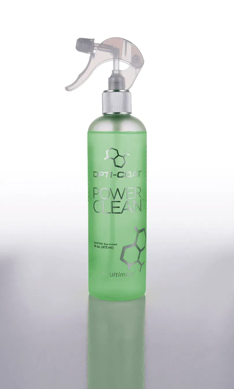 A green spray bottle is sitting on a white surface.