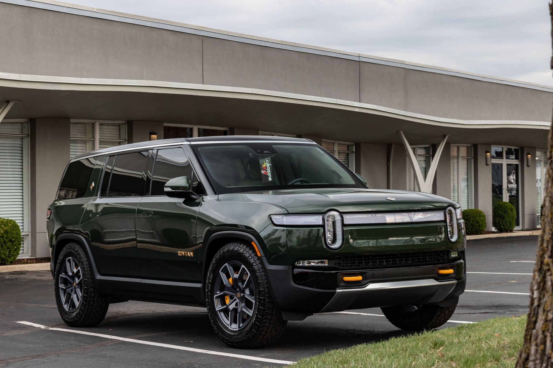 A green suv is parked in a parking lot in front of a building.